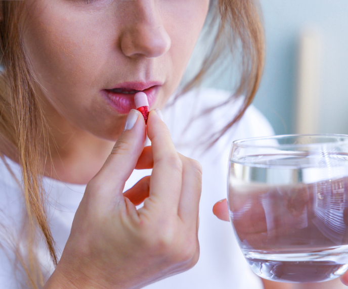 Foto de mulher tomando rem&eacute;dio em copo com &aacute;gua